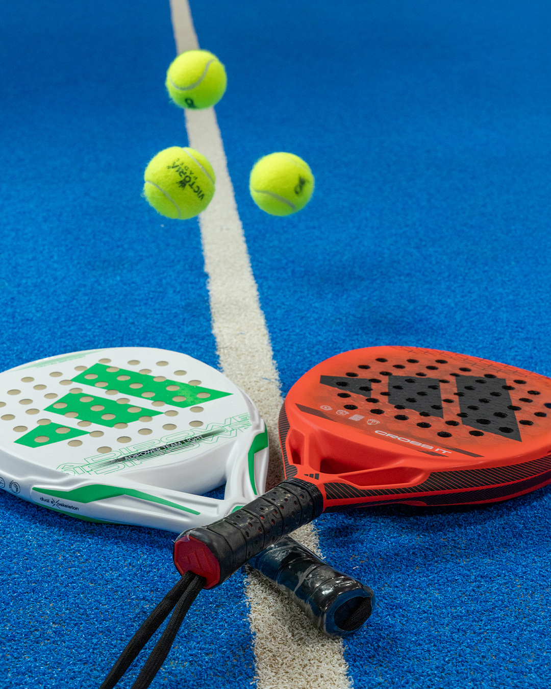 Dos palas de pádel y pelotas sobre una cancha azul